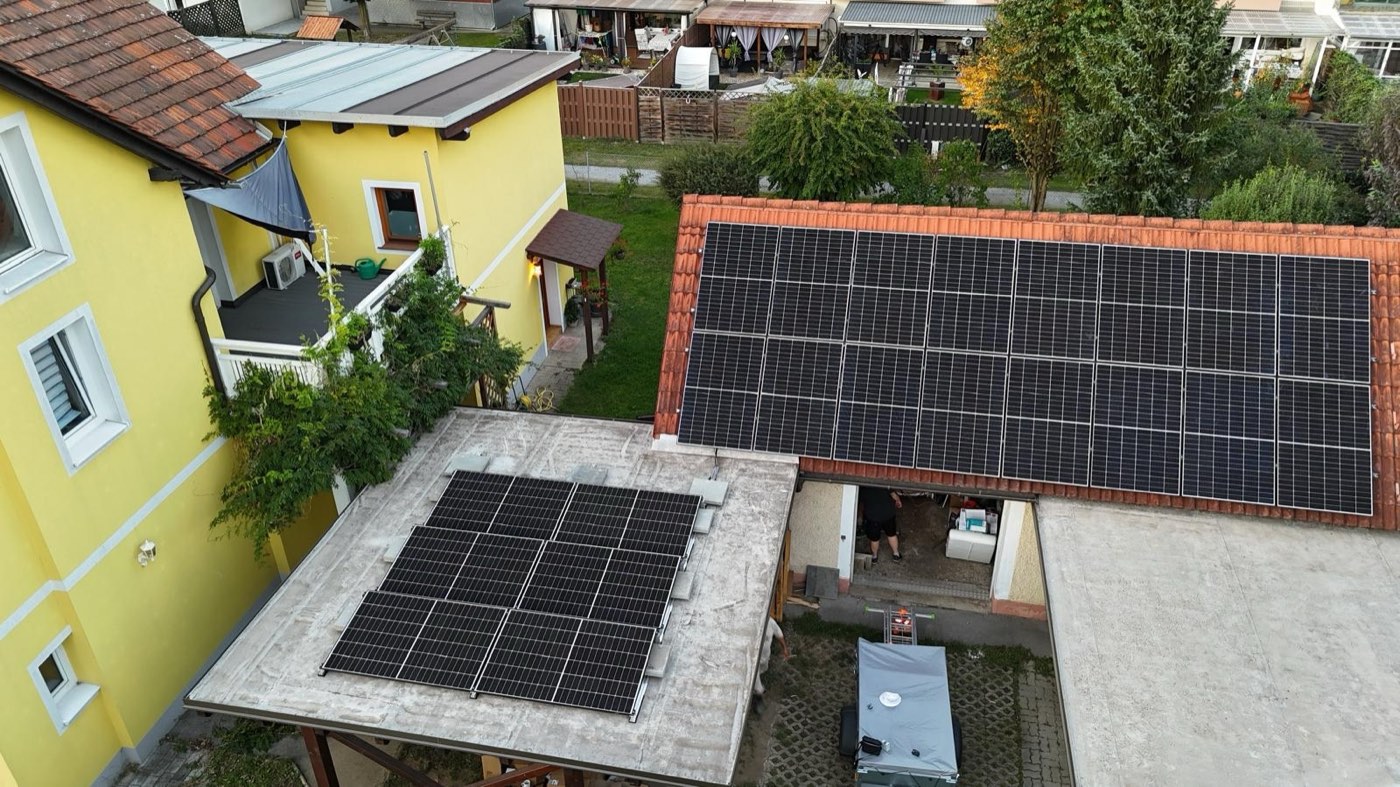 Luftaufnahme einer Solargen-Montage: PV-Module auf einem Ziegeldach und auf dem Flachdach des Carports darunter