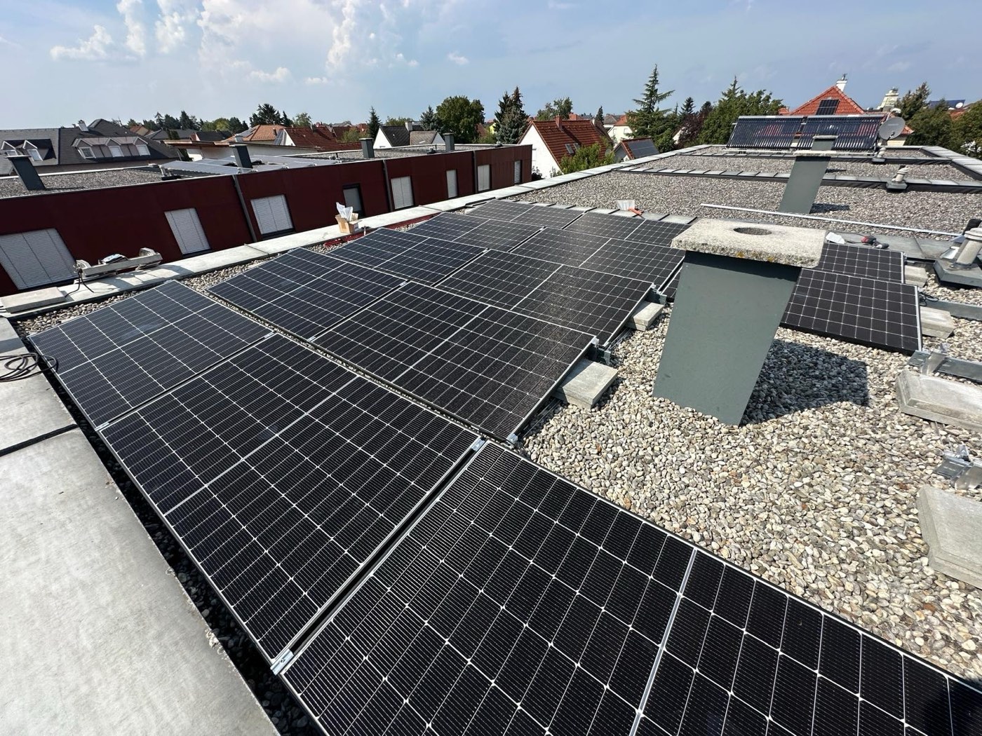Aufgeständerte PV-Module auf einem Kies-Flachdach mit Blick über die Dächer der Siedlung